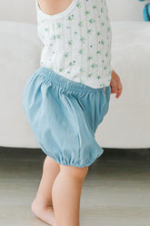 Close-up of toddler wearing Avauma Linen Bloomer Sky. Child sitting down in a floral tank top and light blue linen bloomers.